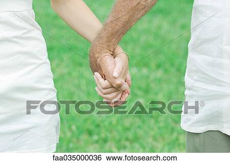 Stock Photograph - Granddaughter and grandfather holding hands outdoors, cropped view. Fotosearch