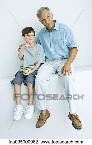 Grandfather and grandson sitting together on ledge, looking away, boy pointing View Large Photo Image Stock Image - Grandfather and grandson sitting together on ledge, looking away, boy pointing. Fotosearch