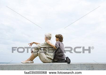 Grandmother and grandson sitting together on low wall outdoors, looking at view View Large Photo Image Stock Photo - Grandmother and grandson sitting together on low wall outdoors, looking at view. Fotosearch