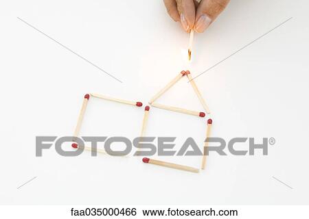 Stock Photograph - Hand holding lit match to house made of matches. Fotosearch