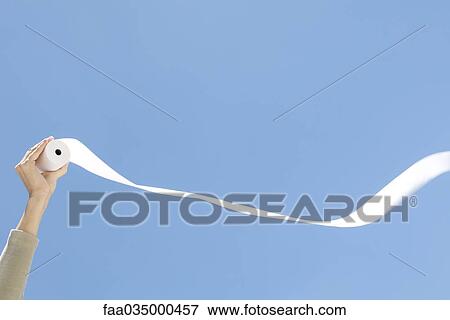 Stock Photo - Hand holding up roll of paper, blue sky in background. Fotosearch