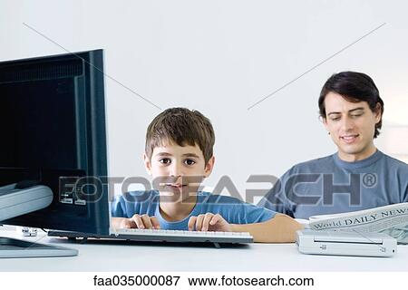 Little boy using computer, smiling at camera, father reading newspaper in background View Large Photo Image Stock Photo - Little boy using computer, smiling at camera, father reading newspaper in background. Fotosearch