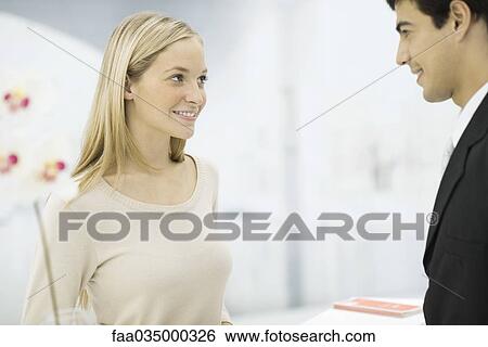 Stock Photograph - Man and woman face to face at counter, smiling at one another. Fotosearch