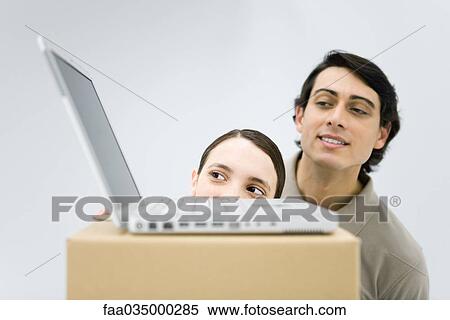 Man and woman peeking at laptop computer sitting on top of cardboard box View Large Photo Image Stock Photography - Man and woman peeking at laptop computer sitting on top of cardboard box. Fotosearch