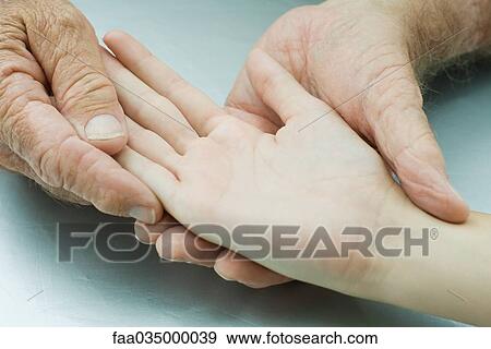 Stock Photo - Man holding young person's hand, palm facing up, cropped view. Fotosearch