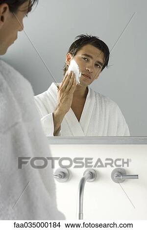 Picture - Man looking at himself in mirror, applying shaving cream. Fotosearch