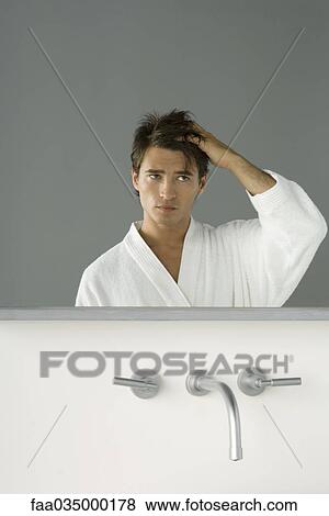 Stock Photo - Man looking at self in mirror, running hand through hair. Fotosearch