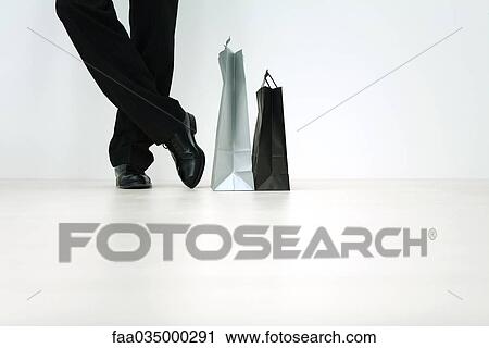 Stock Image - Man standing next to shopping bags, cropped view of feet, low angle view. Fotosearch