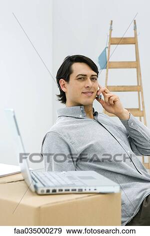 Man using cell phone, smiling at camera, laptop computer sitting on cardboard box in foreground View Large Photo Image Stock Photo - Man using cell phone, smiling at camera, laptop computer sitting on cardboard box in foreground. Fotosearch