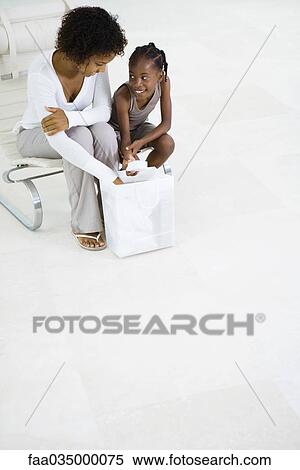 Stock Photography - Mother and daughter exploring contents of shopping bag, smiling. Fotosearch