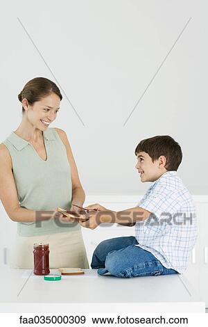 Stock Photo - Mother and son preparing bread and jam together, smiling at each other. Fotosearch