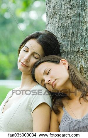 Mother and teen daughter leaning against tree with eyes closed, daughter's head on mother's shoulder View Large Photo Image Picture - Mother and teen daughter leaning against tree with eyes closed, daughter's head on mother's shoulder. Fotosearch