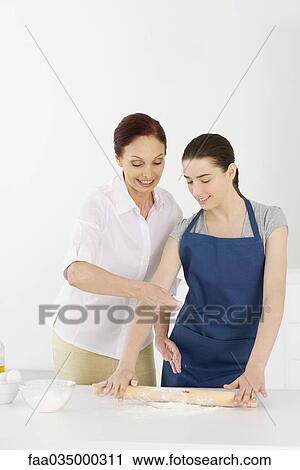 Stock Image - Mother and teen daughter rolling out dough together. Fotosearch
