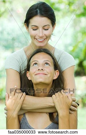 Mother embracing teen daughter from behind, both smiling at each other View Large Photo Image Stock Image - Mother embracing teen daughter from behind, both smiling at each other. Fotosearch