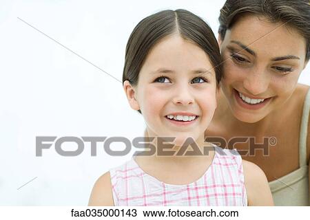Stock Image - Mother leaning over daughter's shoulder, both smiling, portrait. Fotosearch