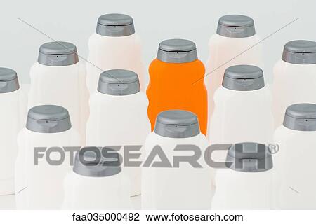 Stock Image - One orange bottle among group of white plastic bottles. Fotosearch