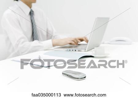 Professional using laptop computer at desk, focus on cell phone in foreground, cropped View Large Photo Image Stock Image - Professional using laptop computer at desk, focus on cell phone in foreground, cropped. Fotosearch