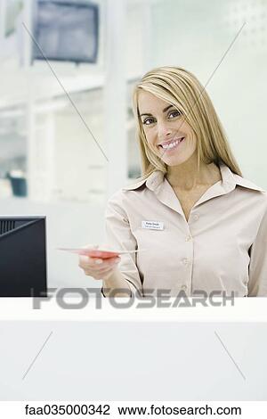 Stock Image - Professional woman holding out brochure, smiling at camera. Fotosearch