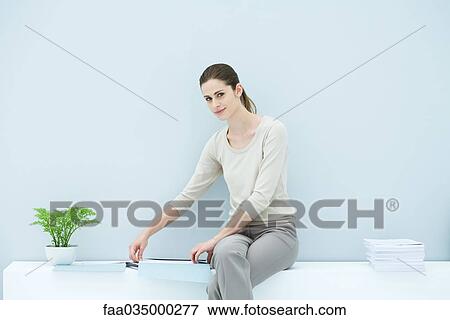 Stock Photo - Professional woman sitting on ledge, organizing documents, smiling at camera. Fotosearch