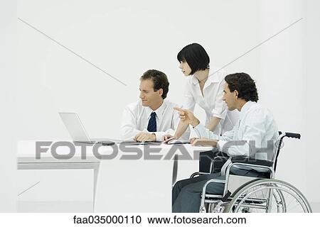 Professionals looking at laptop together, one man sitting in wheelchair View Large Photo Image Stock Image - Professionals looking at laptop together, one man sitting in wheelchair. Fotosearch
