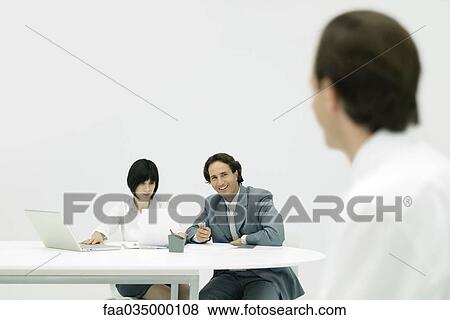 Professionals sitting at desk, woman reading document, man looking at person in foreground View Large Photo Image Stock Photo - Professionals sitting at desk, woman reading document, man looking at person in foreground. Fotosearch