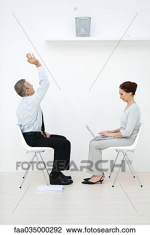 Professionals sitting face to face, man tossing paper ball into wastebasket, woman using laptop View Large Photo Image Stock Image - Professionals sitting face to face, man tossing paper ball into wastebasket, woman using laptop. Fotosearch