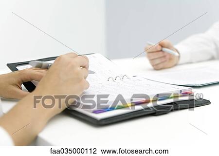 Professionals sitting face to face, one consulting agenda, cropped view View Large Photo Image Stock Image - Professionals sitting face to face, one consulting agenda, cropped view. Fotosearch