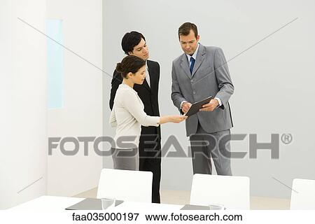 Stock Photo - Professionals standing in conference room, looking down at folder. Fotosearch