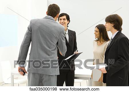 Stock Photo - Professionals standing in conference room, businessmen shaking hands. Fotosearch