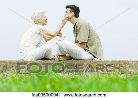 Stock Image - Senior woman and adult son sitting face to face outdoors, sharing take-out food. Fotosearch