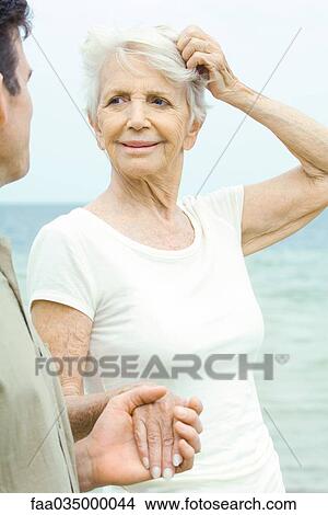 Senior woman scratching head and holding adult son's hand, sea in background View Large Photo Image Picture - Senior woman scratching head and holding adult son's hand, sea in background. Fotosearch
