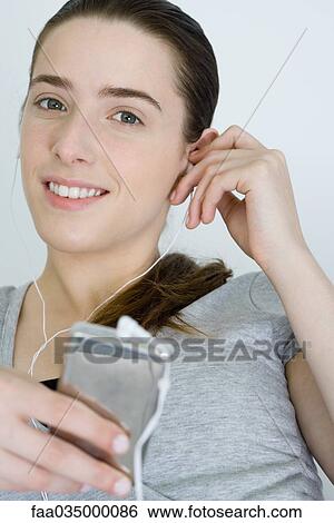 Stock Photograph - Teen girl listening to MP3 player, smiling at camera. Fotosearch
