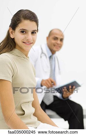 Teenage girl smiling at camera, doctor holding folder in background View Large Photo Image Stock Photography - Teenage girl smiling at camera, doctor holding folder in background. Fotosearch