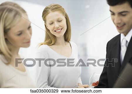 Three professionals looking at folder together, focus on woman smiling in center View Large Photo Image Stock Photo - Three professionals looking at folder together, focus on woman smiling in center. Fotosearch
