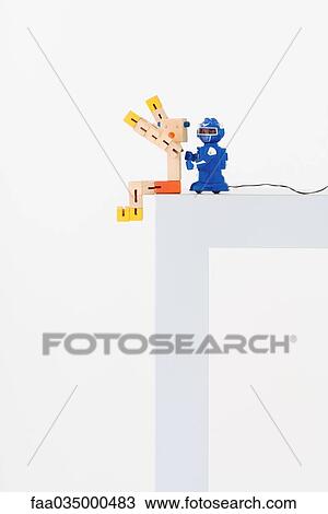 Stock Image - Toy robot pushing wooden toy off edge of table. Fotosearch