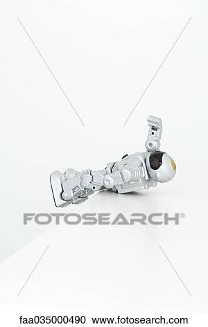 Stock Image - Toy robot resting precariously on edge of table. Fotosearch