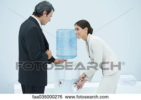Two professionals chatting beside water cooler, woman filling disposable cup View Large Photo Image Stock Photograph - Two professionals chatting beside water cooler, woman filling disposable cup. Fotosearch