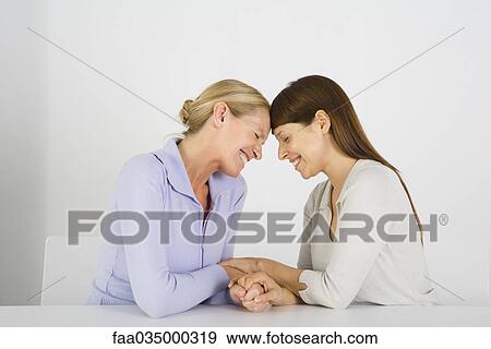 Stock Photo - Two women holding hands, touching foreheads, eyes closed. Fotosearch