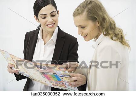 Stock Image - Two women looking at travel brochure together. Fotosearch