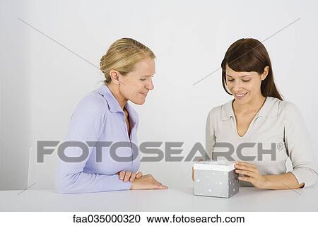 Two women sitting at table, one opening gift, both smiling View Large Photo Image Stock Image - Two women sitting at table, one opening gift, both smiling. Fotosearch