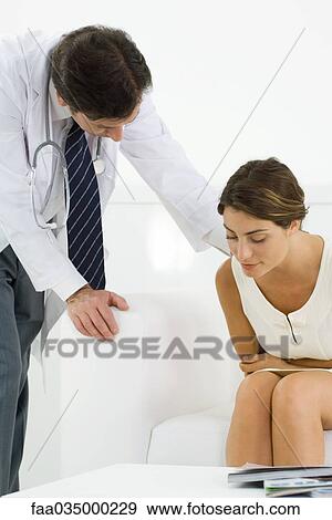 Woman bending over, holding stomach, doctor leaning over to check on her View Large Photo Image Stock Photo - Woman bending over, holding stomach, doctor leaning over to check on her. Fotosearch