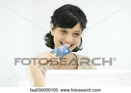 Woman biting edge of credit card, smiling down at laptop View Large Photo Image Stock Image - Woman biting edge of credit card, smiling down at laptop. Fotosearch