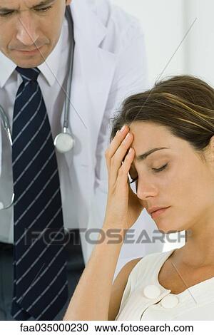 Stock Image - Woman holding head, doctor leaning behind her. Fotosearch