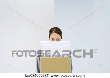 Stock Photo - Woman peeking over stack of paper on top of cardboard box. Fotosearch