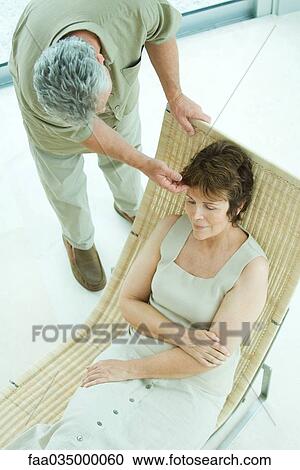 Stock Image - Woman relaxing on lounge chair, husband bending over to touch her hair. Fotosearch