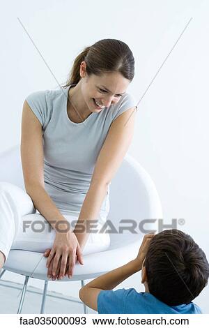 Stock Image - Woman sitting in chair, smiling down at son. Fotosearch