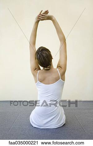 Stock Image - Woman sitting on the floor, stretching arms, rear view. Fotosearch