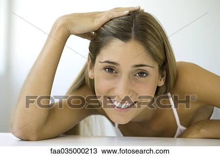 Stock Image - Woman smiling at camera, hand on head, portrait. Fotosearch