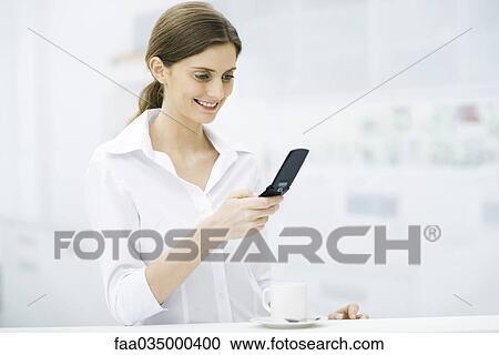 Woman standing at kitchen counter, looking at cell phone, smiling View Large Photo Image Stock Image - Woman standing at kitchen counter, looking at cell phone, smiling. Fotosearch