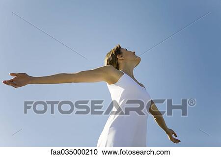 Stock Image - Woman with outstretched arms, looking up, low angle view. Fotosearch